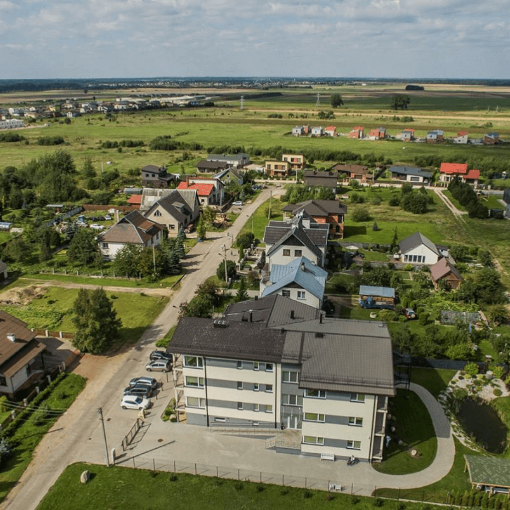 Aerialinė gyvenamojo rajono panorama su daugiabučiu, individualiais namais ir žaliuojančiomis apylinkėmis