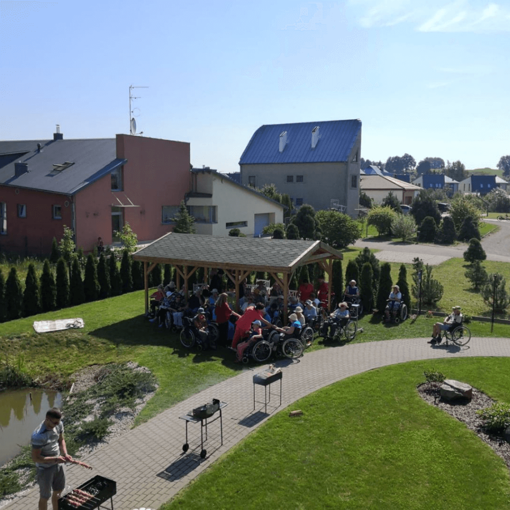 Globos namų gyventojai leidžia laiką lauke pavėsinėje, vyksta bendruomenės susitikimas kiemo teritorijoje