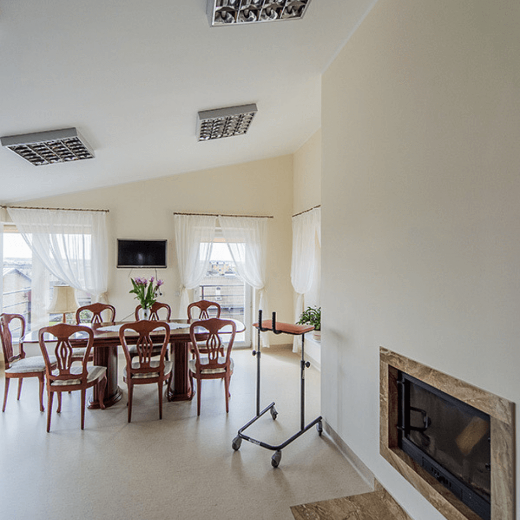 Jauki globos namų bendroji erdvė su valgomojo stalu, kėdėmis, židiniu ir vaikštyne prie lango