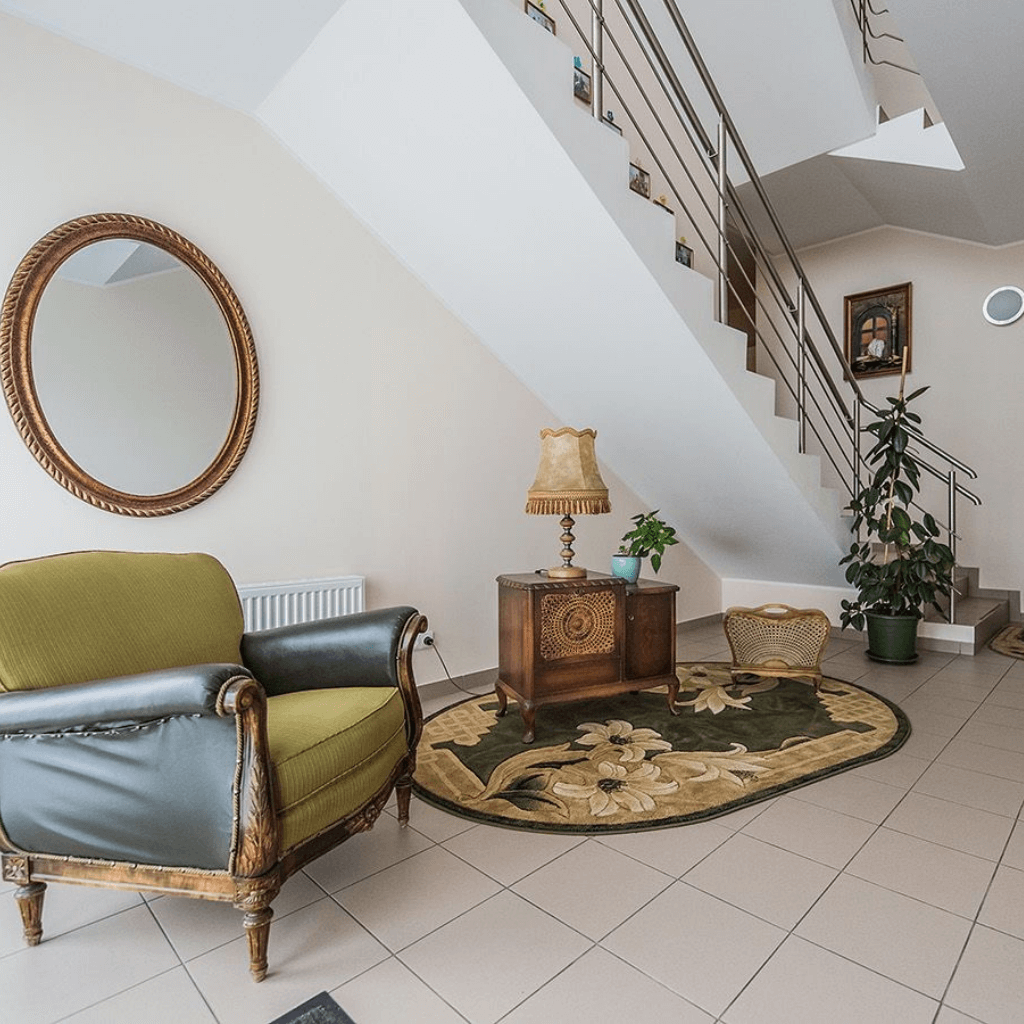 Jauki pastato holas su laiptais, klasikiniu foteliu ir dekoratyvinėmis interjero detalėmis.