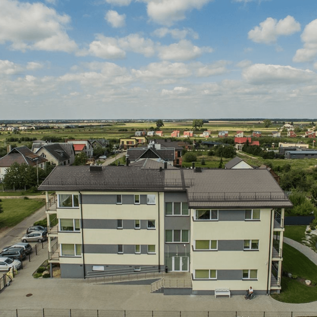 Modernus daugiabutis gyvenamajame rajone su tvarkinga aplinka ir žaliuojančiais laukais fone