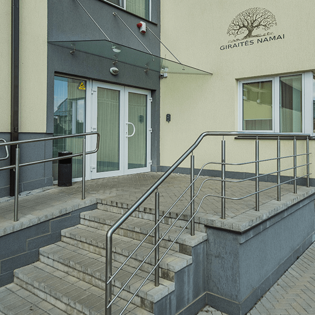 Modernus pastato įėjimas su stiklinėmis durimis, turėklais ir pritaikytu pandusu patogiam patekimui
